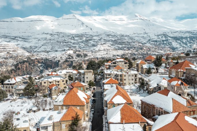 Hasroun Lebanon Snow-covered rooftops with orange tiles overlook a snowy mountainous landscape.