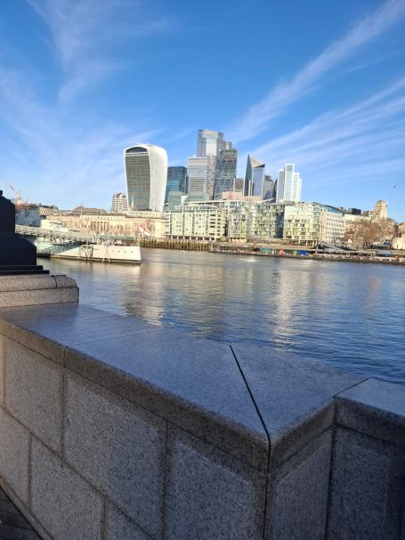 London City skyline reflecting on a river, with modern buildings under a clear blue sky.